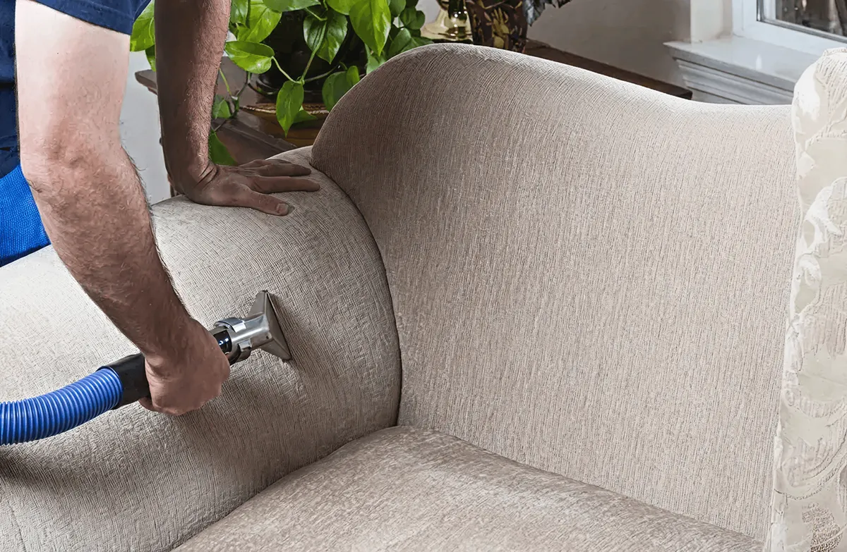 Professional upholstery cleaner deep-cleaning a fabric sofa with a handheld extraction tool and hose, Peoria, IL.